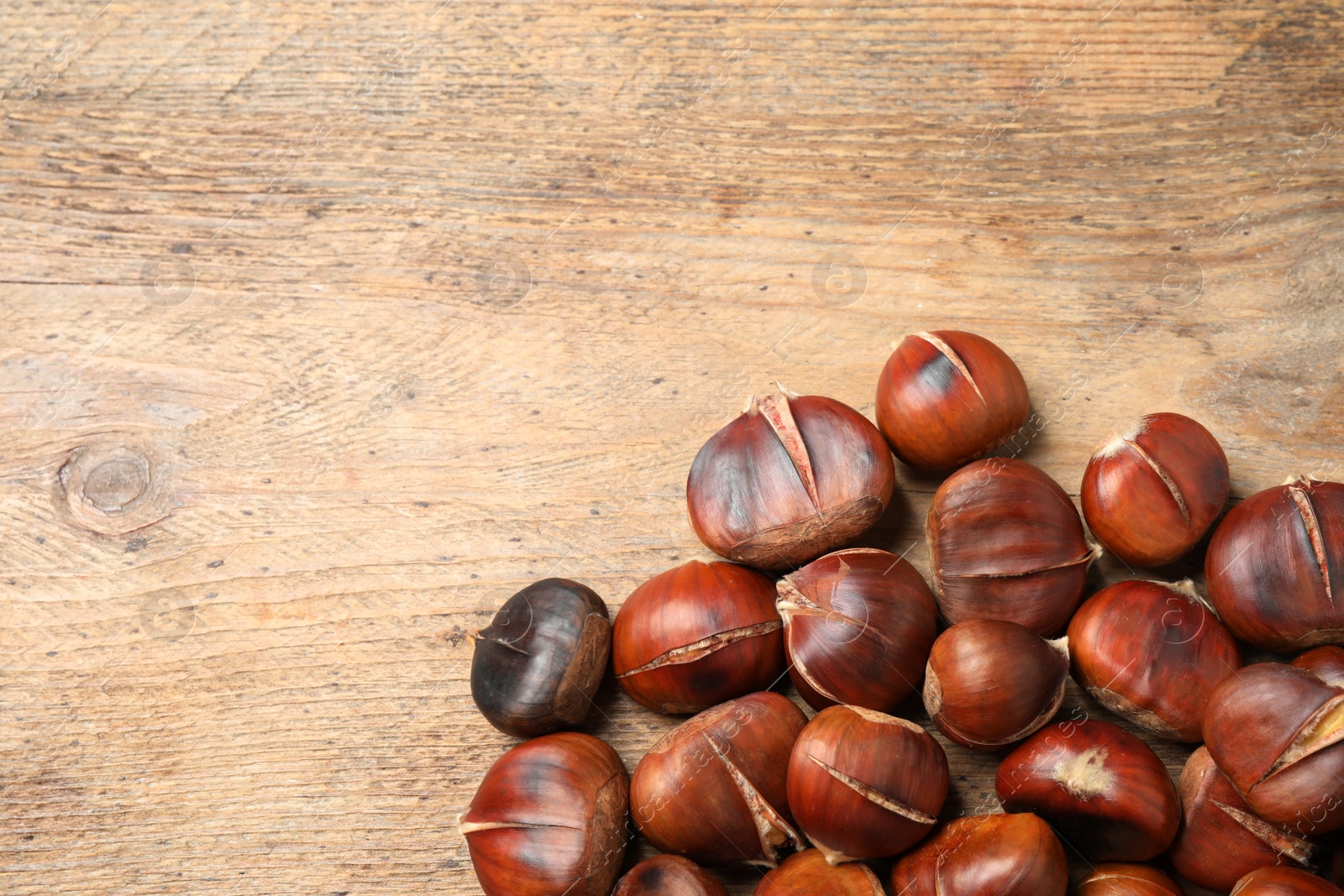 Photo of Delicious roasted edible chestnuts on wooden table, flat lay. Space for text