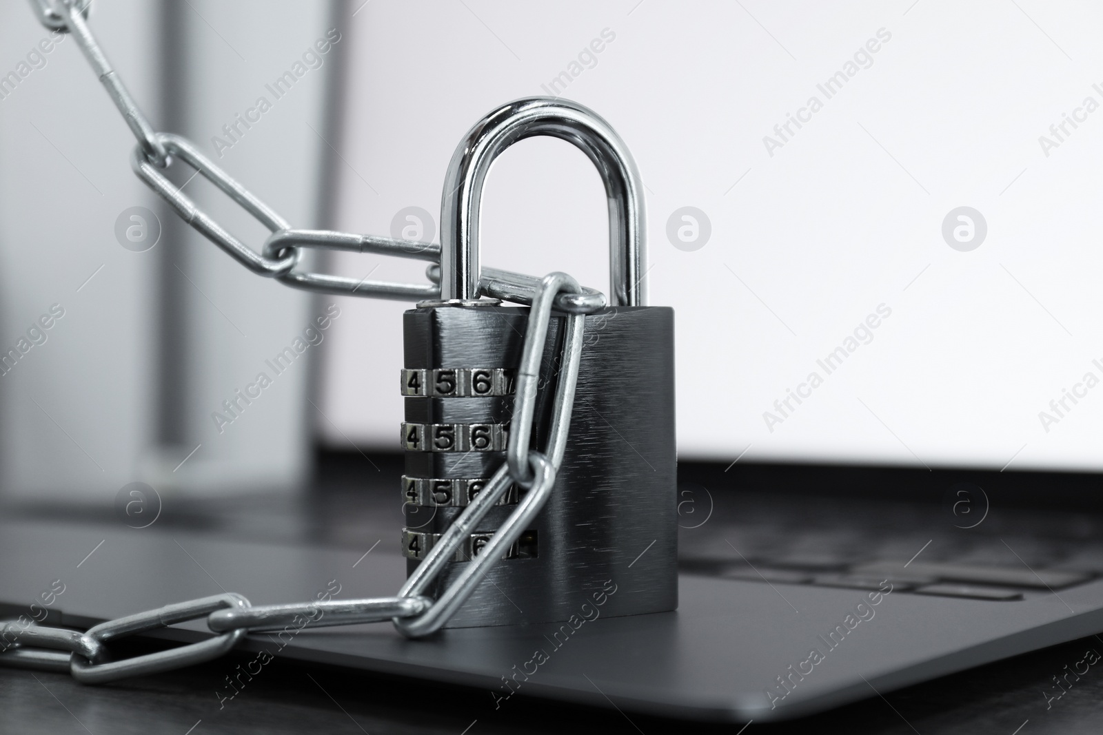 Photo of Cyber security. Metal combination padlock with chain and laptop on table, closeup