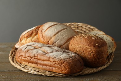 Photo of Wicker basket with different types of fresh bread on wooden table, closeup