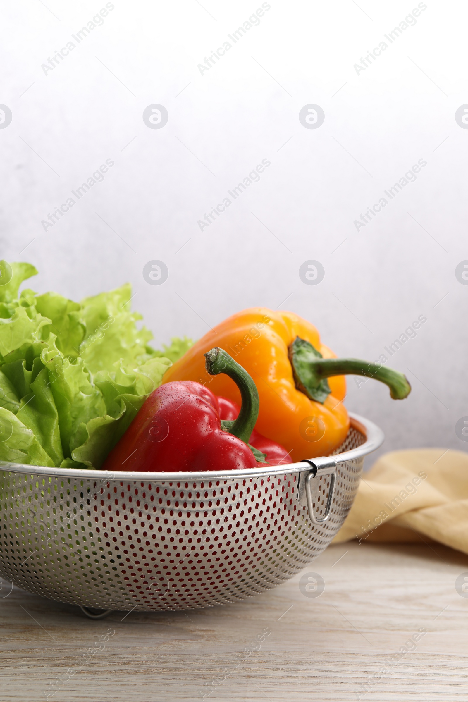 Photo of Colander with fresh lettuce and bell peppers on wooden table