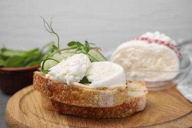 Photo of Tasty sandwich with burrata cheese and cucumber on wooden board, closeup
