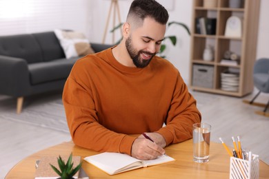 Photo of Young man writing in notebook at wooden table indoors