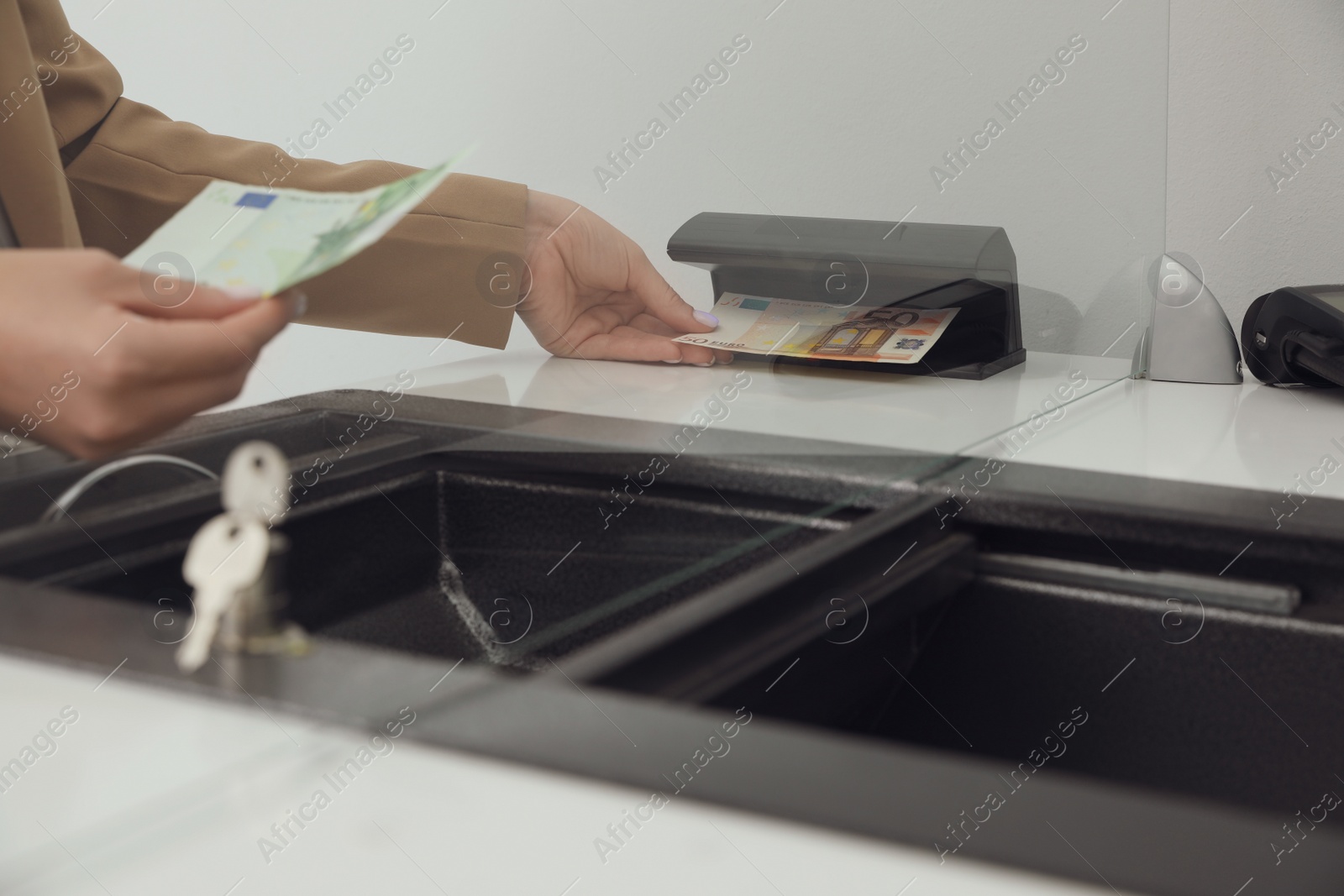 Photo of Cashier checking money with currency detector at exchange department, closeup