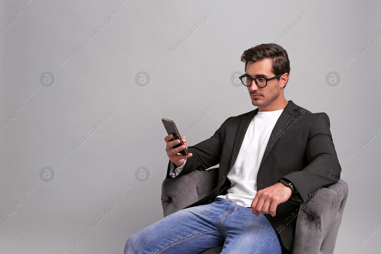 Photo of Handsome young businessman with smartphone sitting in armchair on grey background. Space for text