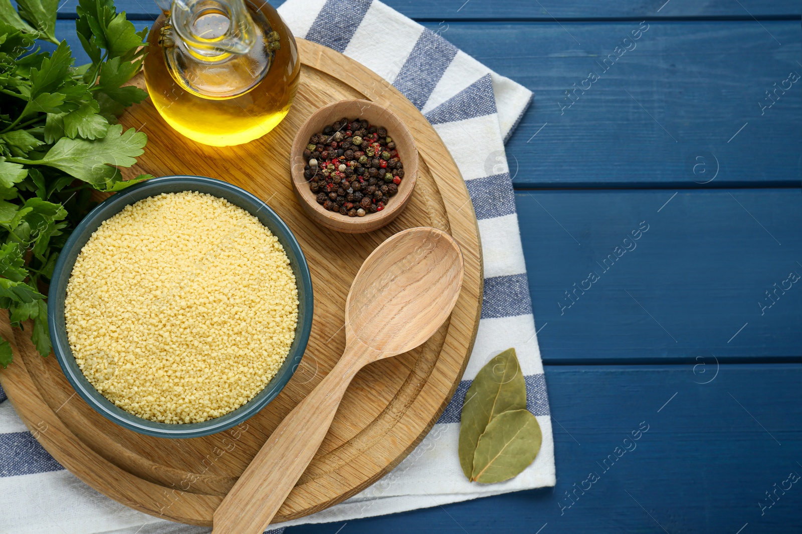 Photo of Bowl of raw couscous and ingredients on blue wooden table, flat lay. Space for text