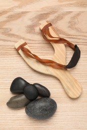 Slingshot with stones on wooden background, flat lay