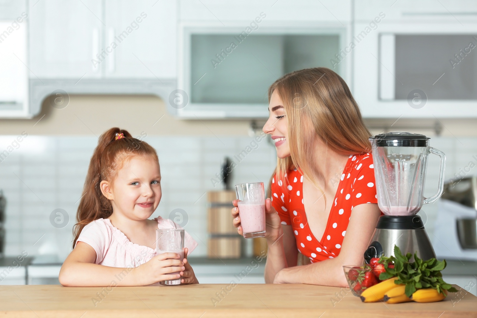 Photo of Young woman and her daughter with glasses of delicious milk shakes in kitchen