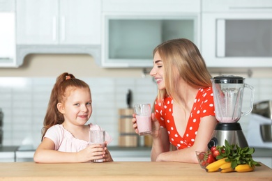 Photo of Young woman and her daughter with glasses of delicious milk shakes in kitchen