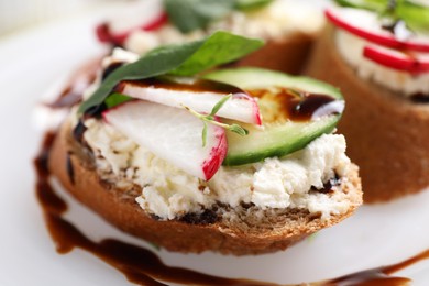 Photo of Delicious bruschettas with cream cheese, vegetables and balsamic vinegar on white plate, closeup