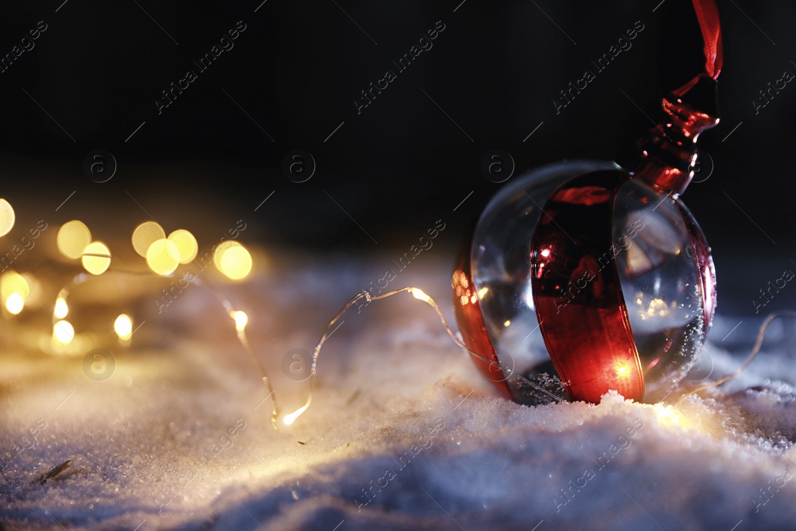 Photo of Christmas ball and fairy lights on white snow outdoors. Space for text