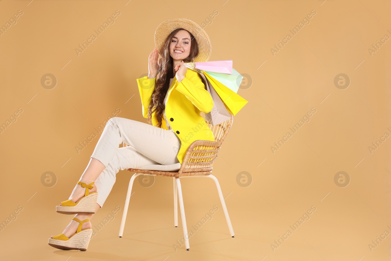 Photo of Happy woman holding many colorful shopping bags on armchair against beige background