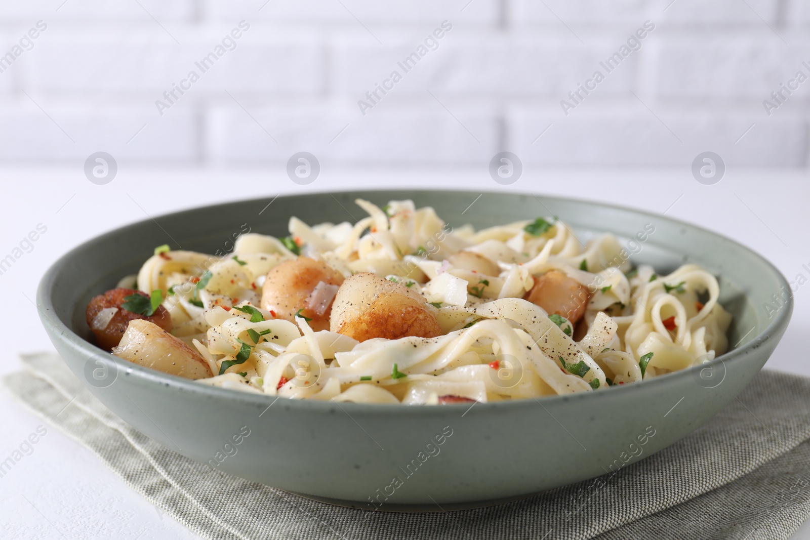 Photo of Delicious scallop pasta with spices in bowl on white table, closeup