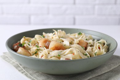 Delicious scallop pasta with spices in bowl on white table, closeup