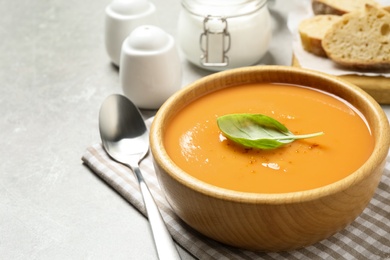 Photo of Tasty creamy pumpkin soup with basil in bowl on grey table