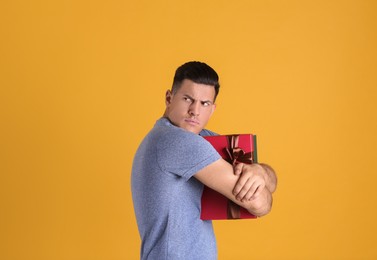 Photo of Greedy man hiding gift box on yellow background, space for text