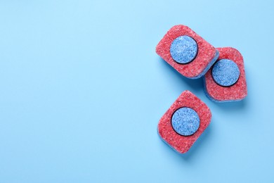 Photo of Dishwasher detergent tablets on light blue background, flat lay. Space for text