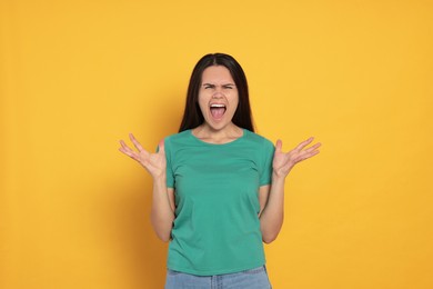 Aggressive young woman shouting on orange background