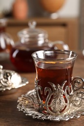Photo of Glass of traditional Turkish tea in vintage holder on wooden table
