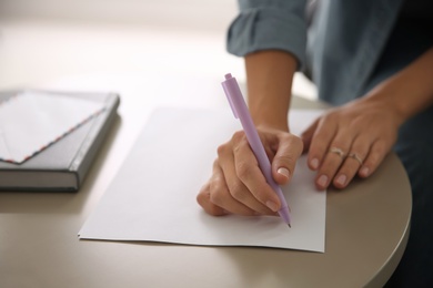 Woman writing letter at table indoors, closeup