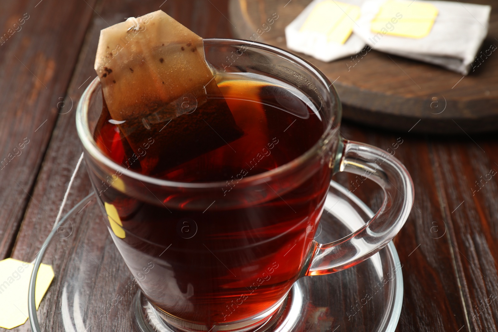 Photo of Brewing tea. Glass cup with tea bag on wooden table, closeup