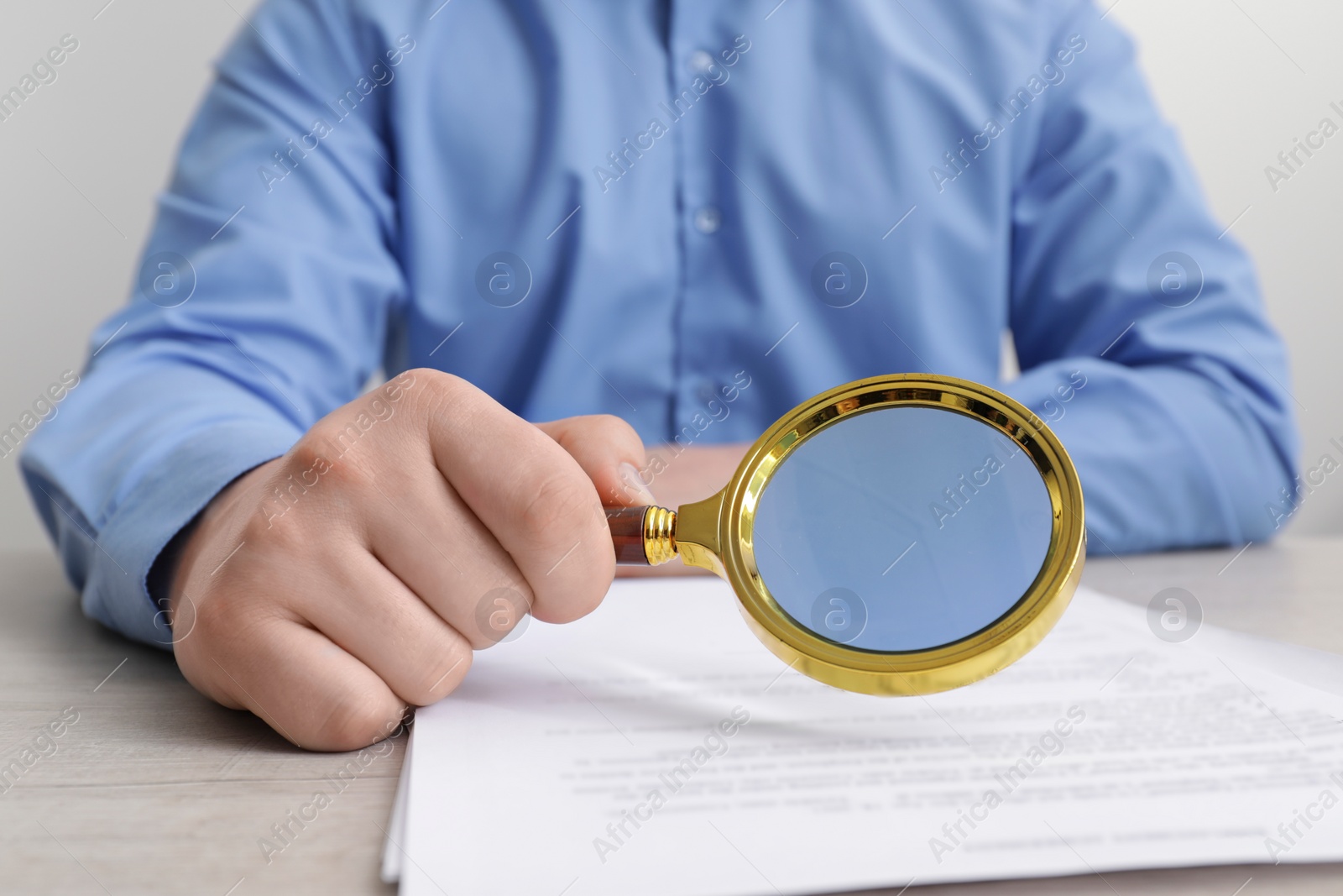 Photo of Man looking at document through magnifier at white wooden table, closeup. Searching concept