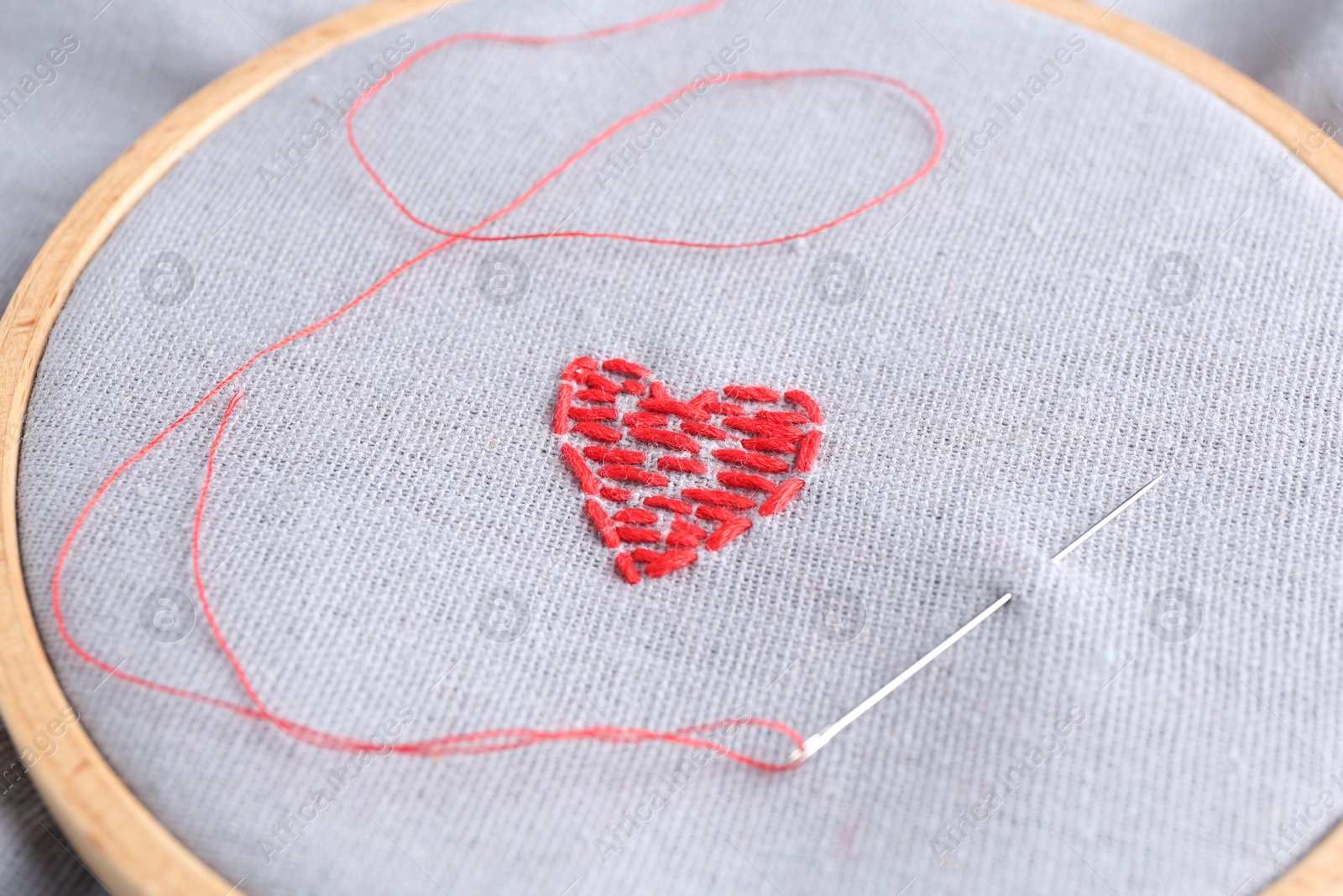 Photo of Embroidered red heart and needle on gray cloth, closeup