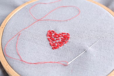 Photo of Embroidered red heart and needle on gray cloth, closeup