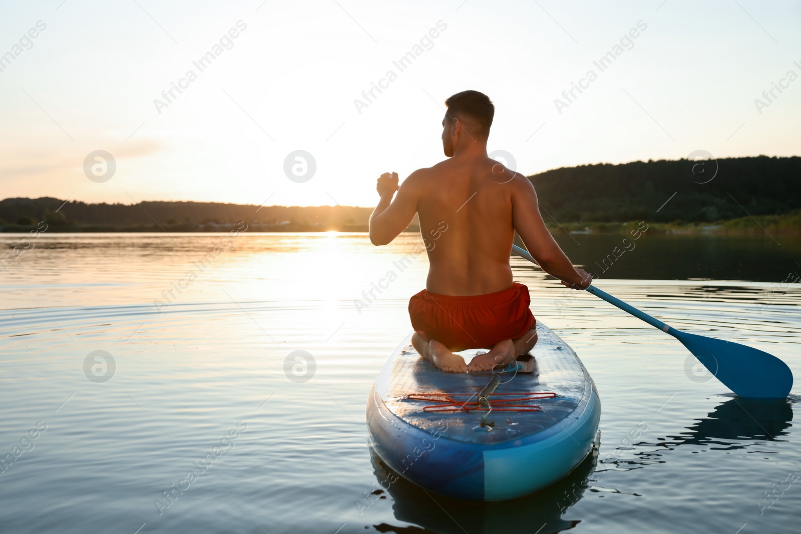 Photo of Man paddle boarding on SUP board in river at sunset, back view