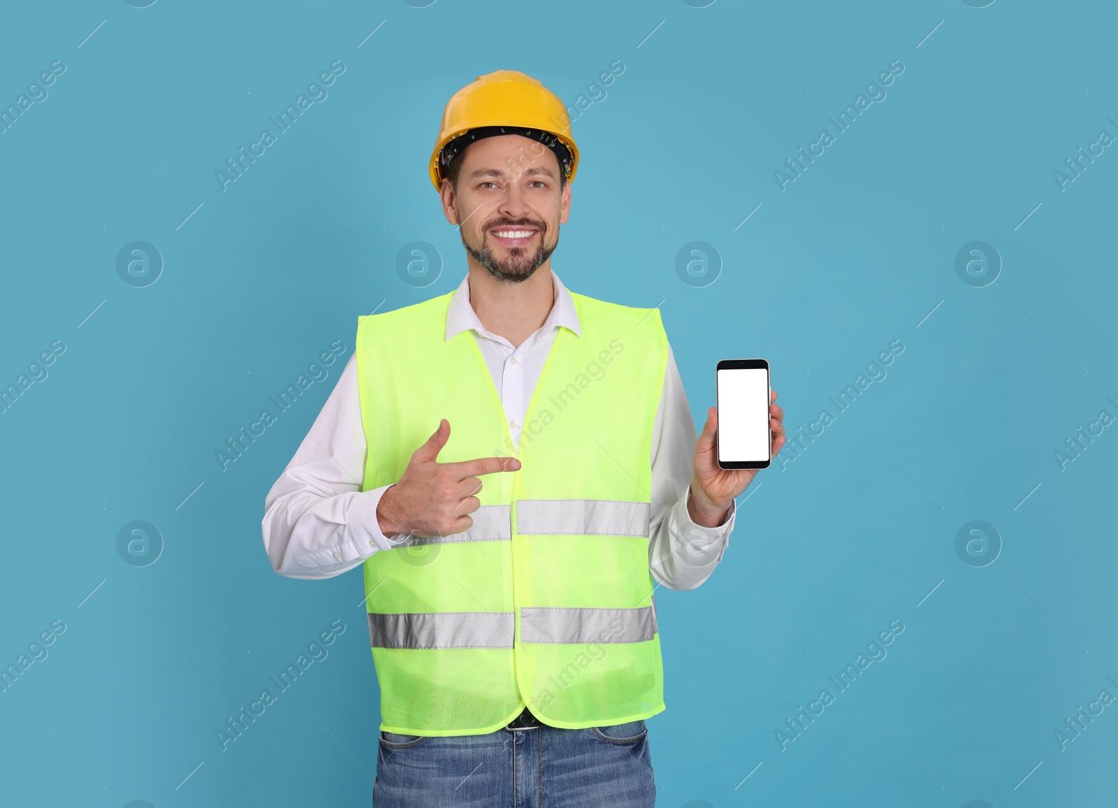 Photo of Male industrial engineer in uniform with phone on light blue background