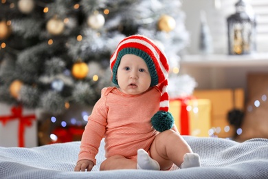 Photo of Little baby wearing elf hat on blanket indoors. First Christmas