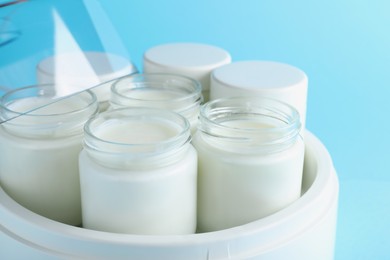 Modern yogurt maker with full jars on light blue background, closeup