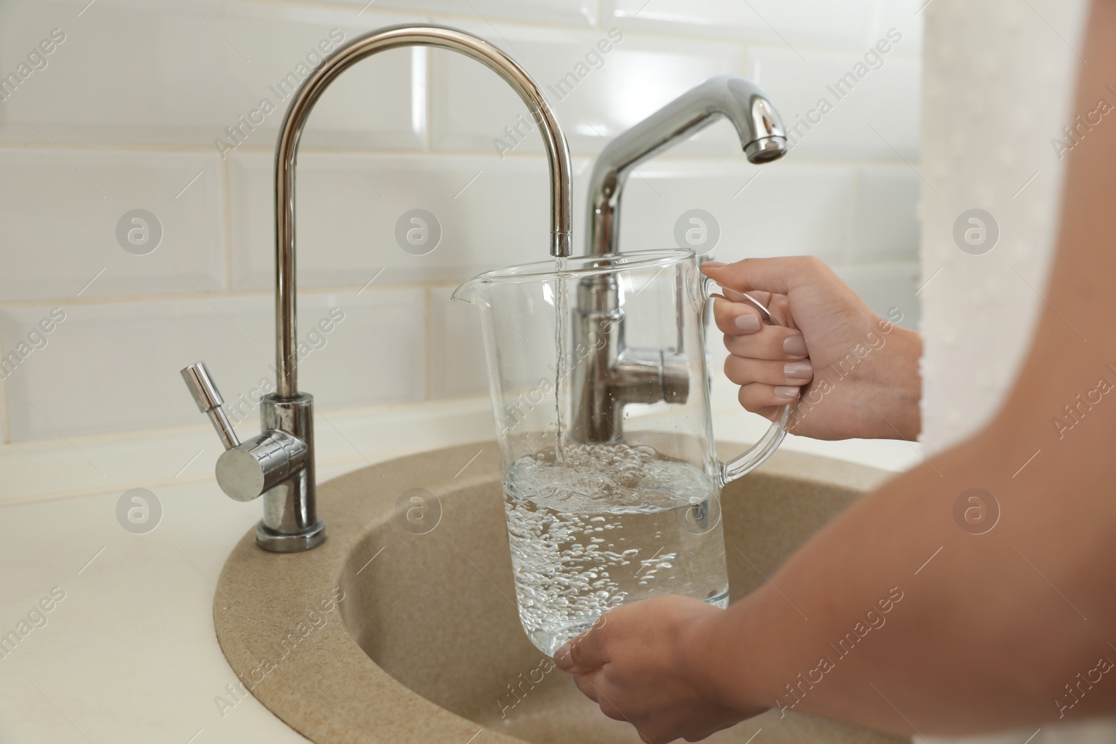 Photo of Woman pouring water into glass jug in kitchen, closeup