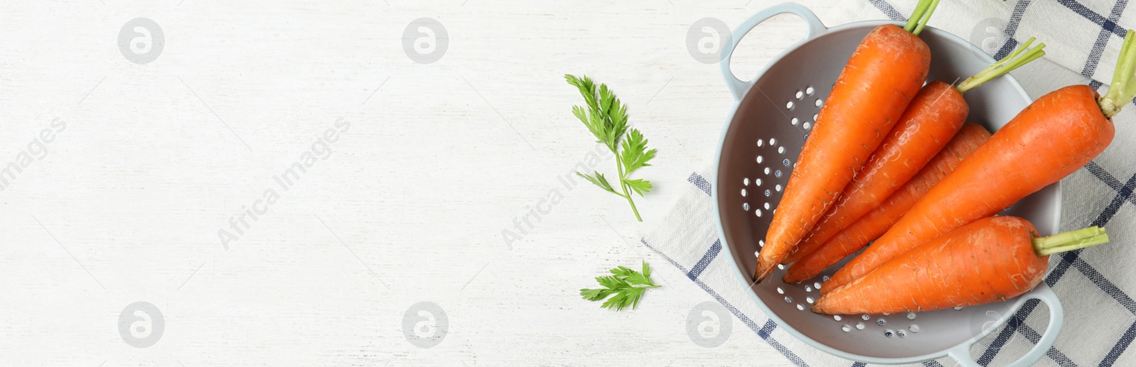 Image of Fresh carrots in colander on white table, top view with space for text. Banner design 