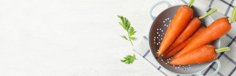 Fresh carrots in colander on white table, top view with space for text. Banner design 