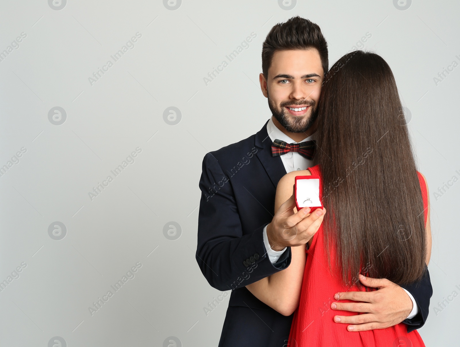 Photo of Man with engagement ring making marriage proposal to girlfriend on light grey background. Space for text
