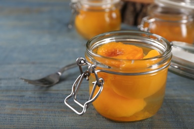 Glass jar with conserved peach halves on wooden table. Space for text