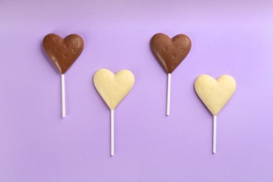 Photo of Different chocolate heart shaped lollipops on light lilac background, flat lay