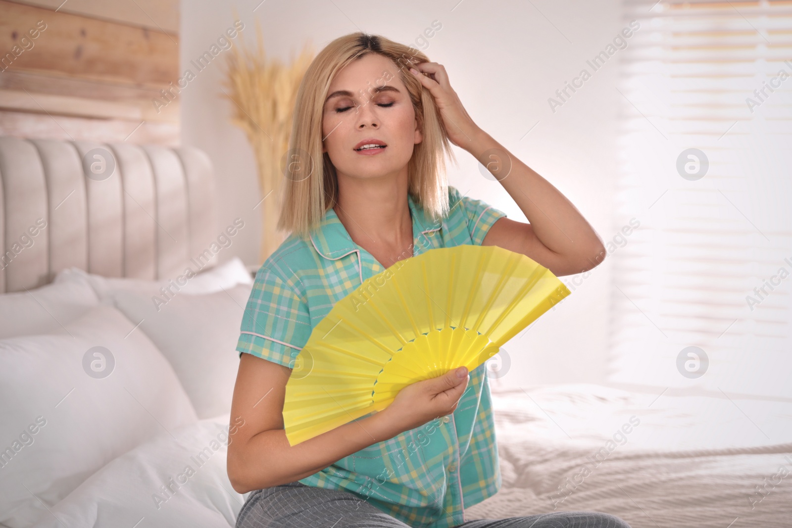 Photo of Woman with hand fan suffering from heat at home. Summer season