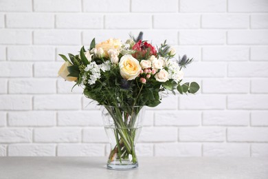 Photo of Beautiful bouquet with roses on grey table against white brick wall