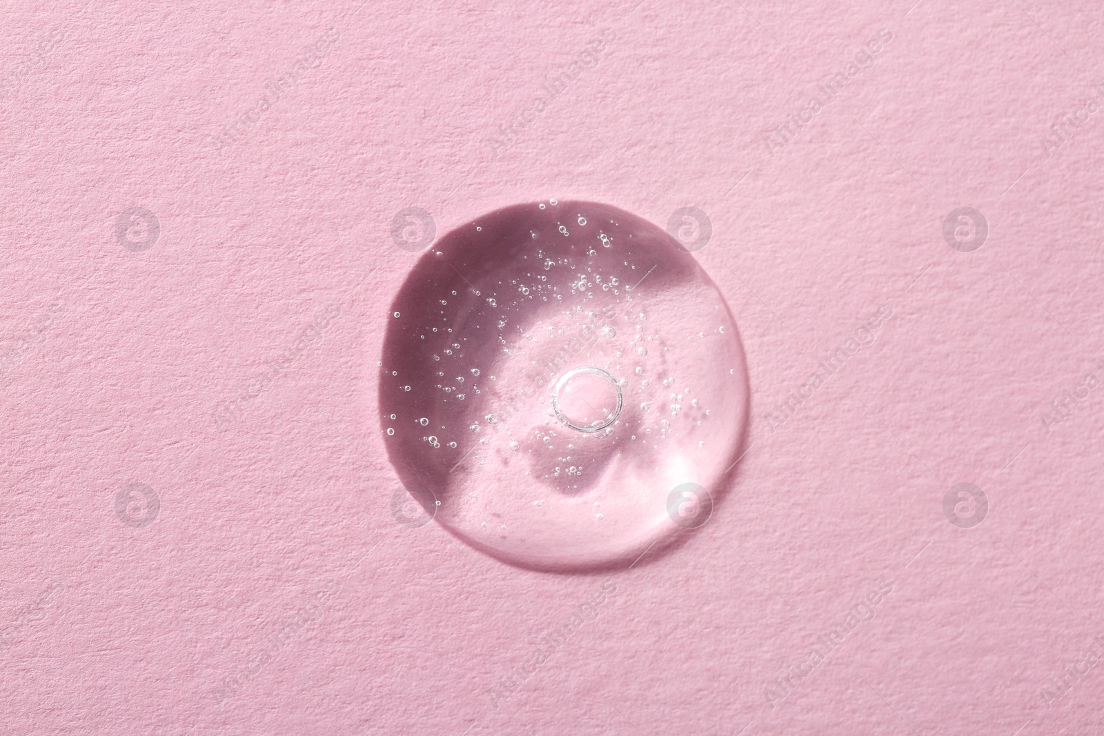 Photo of Drop of cosmetic serum on pink background, top view