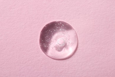 Drop of cosmetic serum on pink background, top view