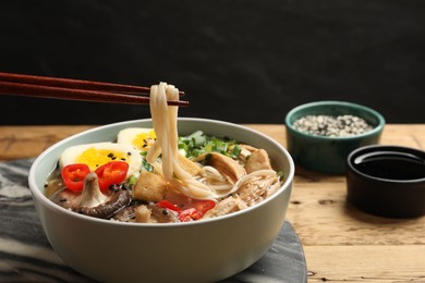 Eating delicious ramen with chopsticks on wooden table, closeup. Noodle soup