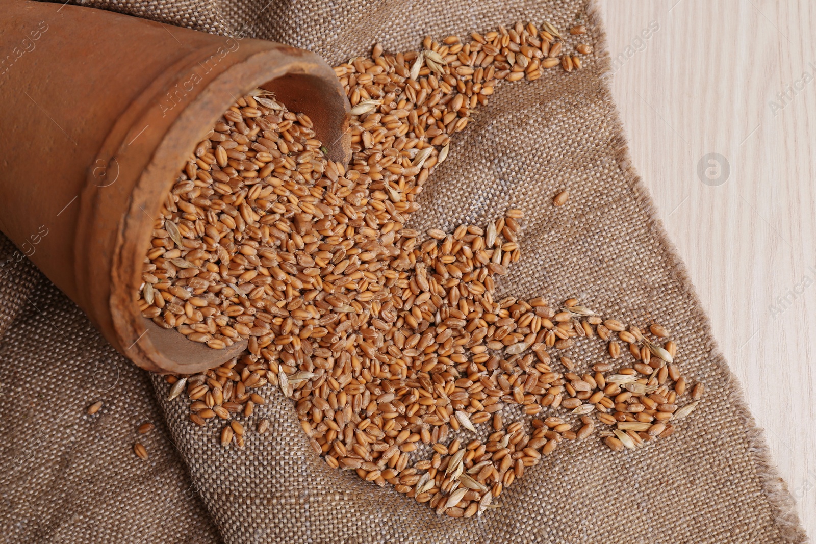 Photo of Overturned pot with scattered wheat grains on white wooden table