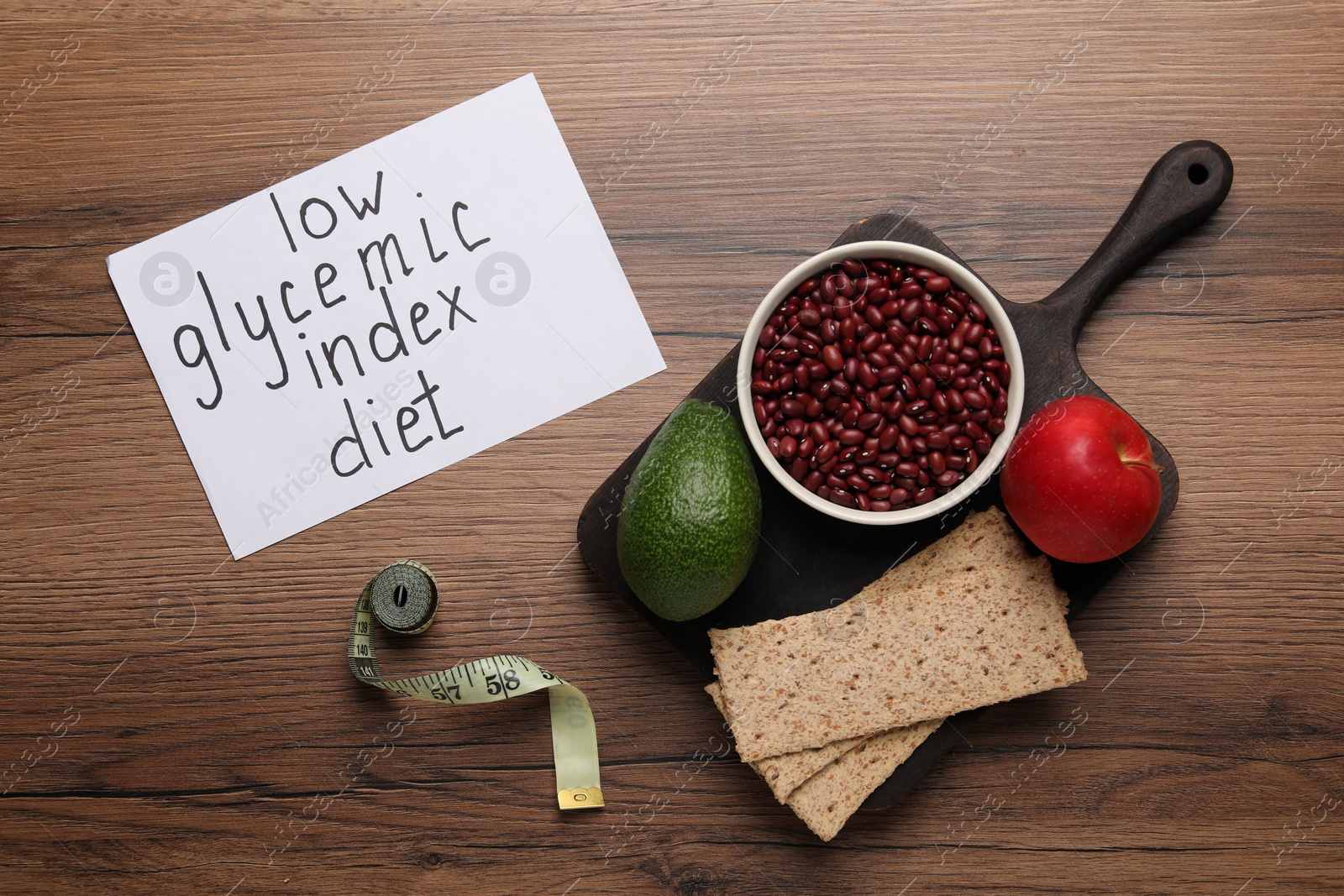 Photo of Paper with words Low Glycemic Index Diet, measuring tape and healthy products on wooden table, flat lay