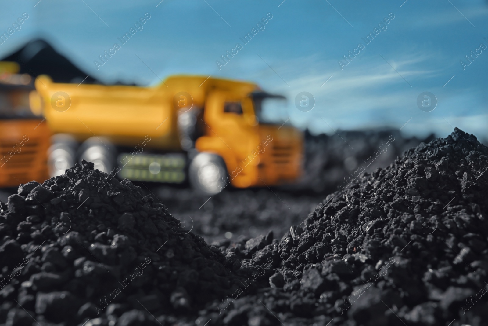 Image of Pile of coal and blurred yellow truck on background, closeup