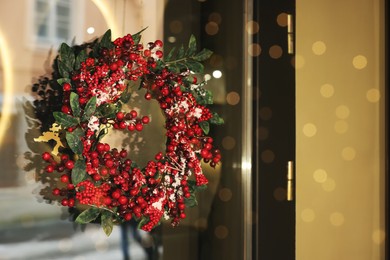 Beautiful Christmas wreath hanging on glass door, space for text