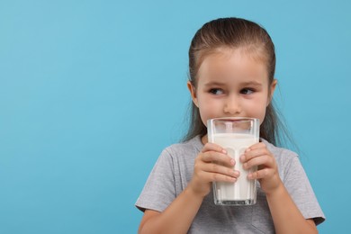 Photo of Cute girl with glass of fresh milk on light blue background, space for text