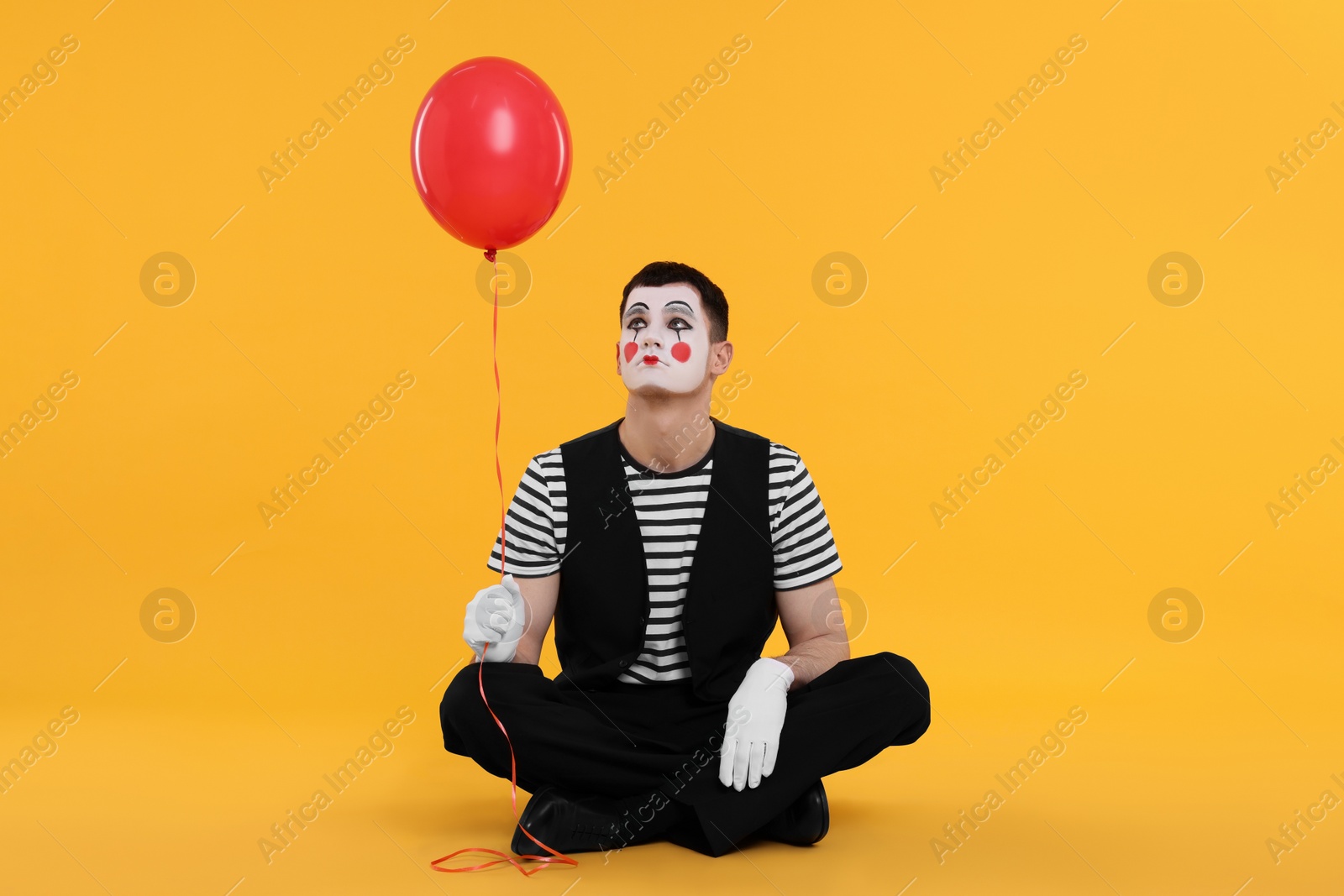 Photo of Funny mime artist with balloon on orange background