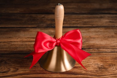 Photo of Golden bell with red bow on wooden table. School days