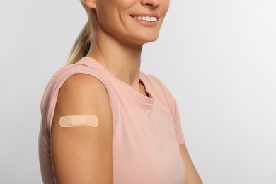 Photo of Smiling woman with adhesive plaster on arm after vaccination on light background, closeup